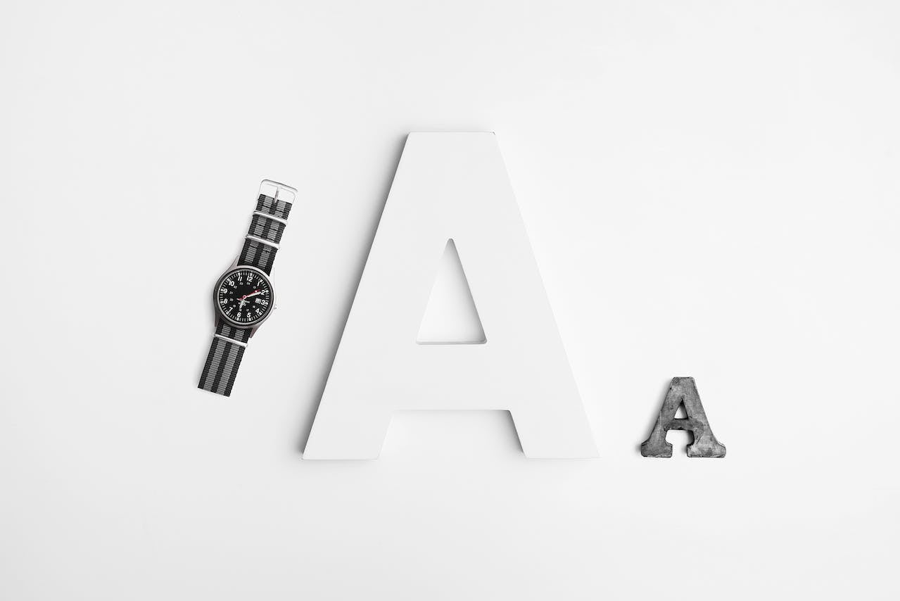 A white background showcasing the letter 'A' and a watch side by side.