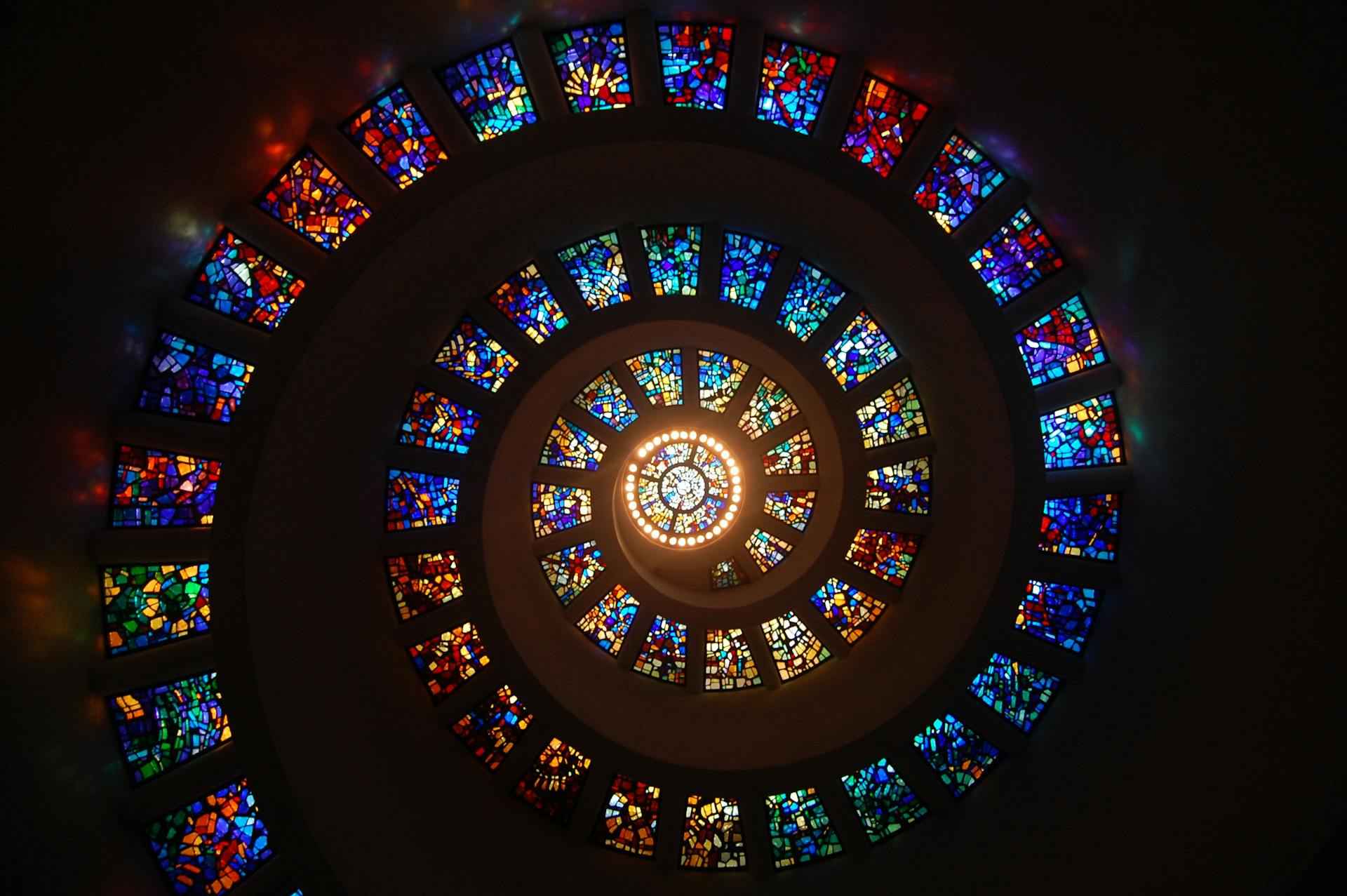 Colorful stained glass spiral ceiling with vibrant patterns, showcasing intricate design and lighting effects.